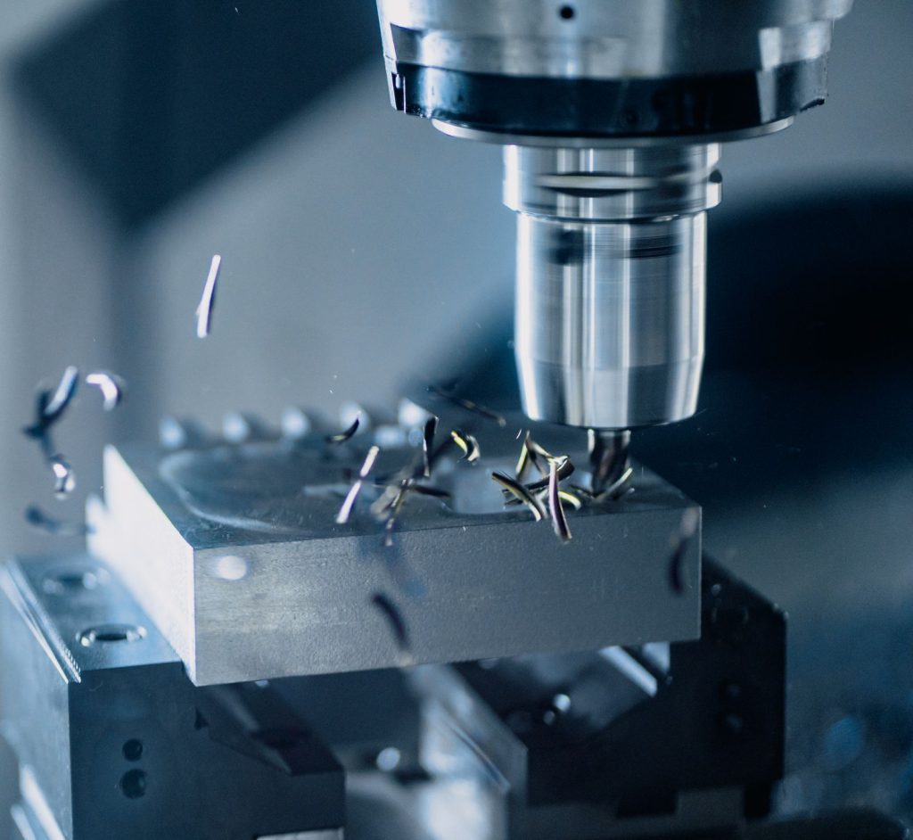 Grande plano de uma fresa CNC a maquinar uma peça de aço, com aparas a saltar