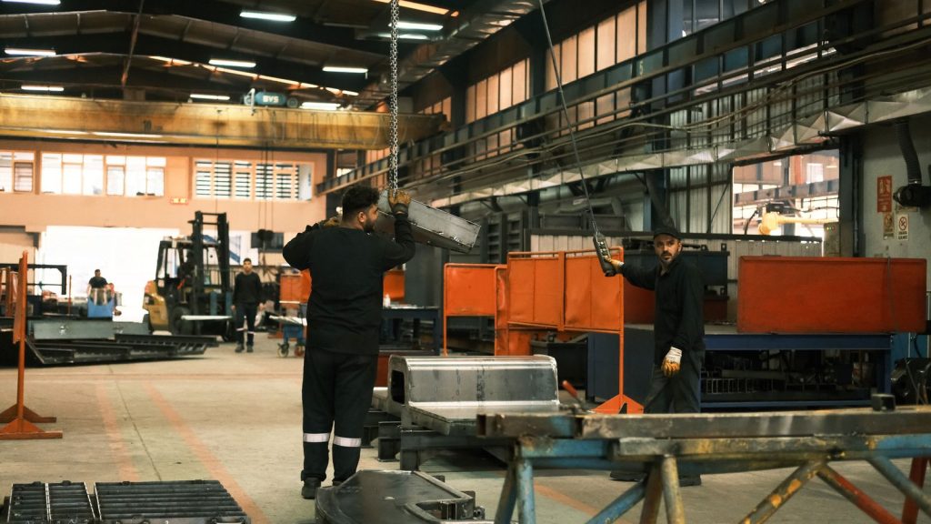 Vista ampla de uma nave de metalomecânica com ponte rolante e operadores em trabalho